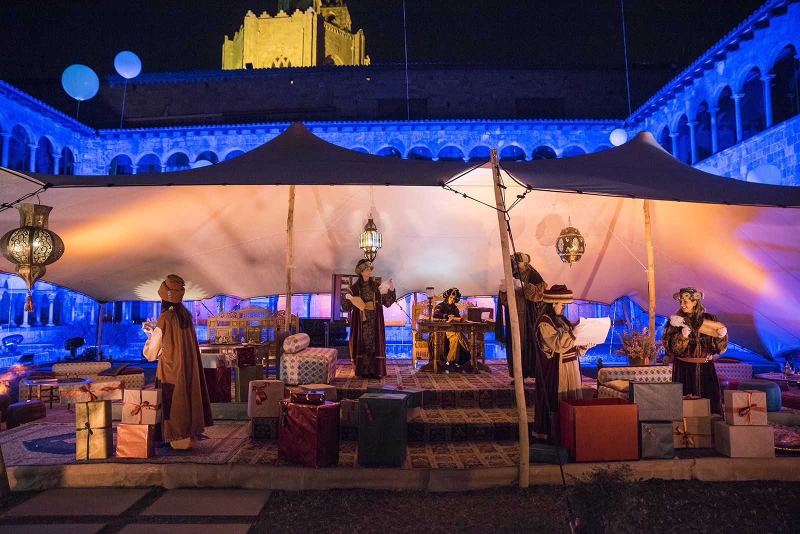 Campament reial nocturn al claustre del monestir, il·luminat de blau i ambre