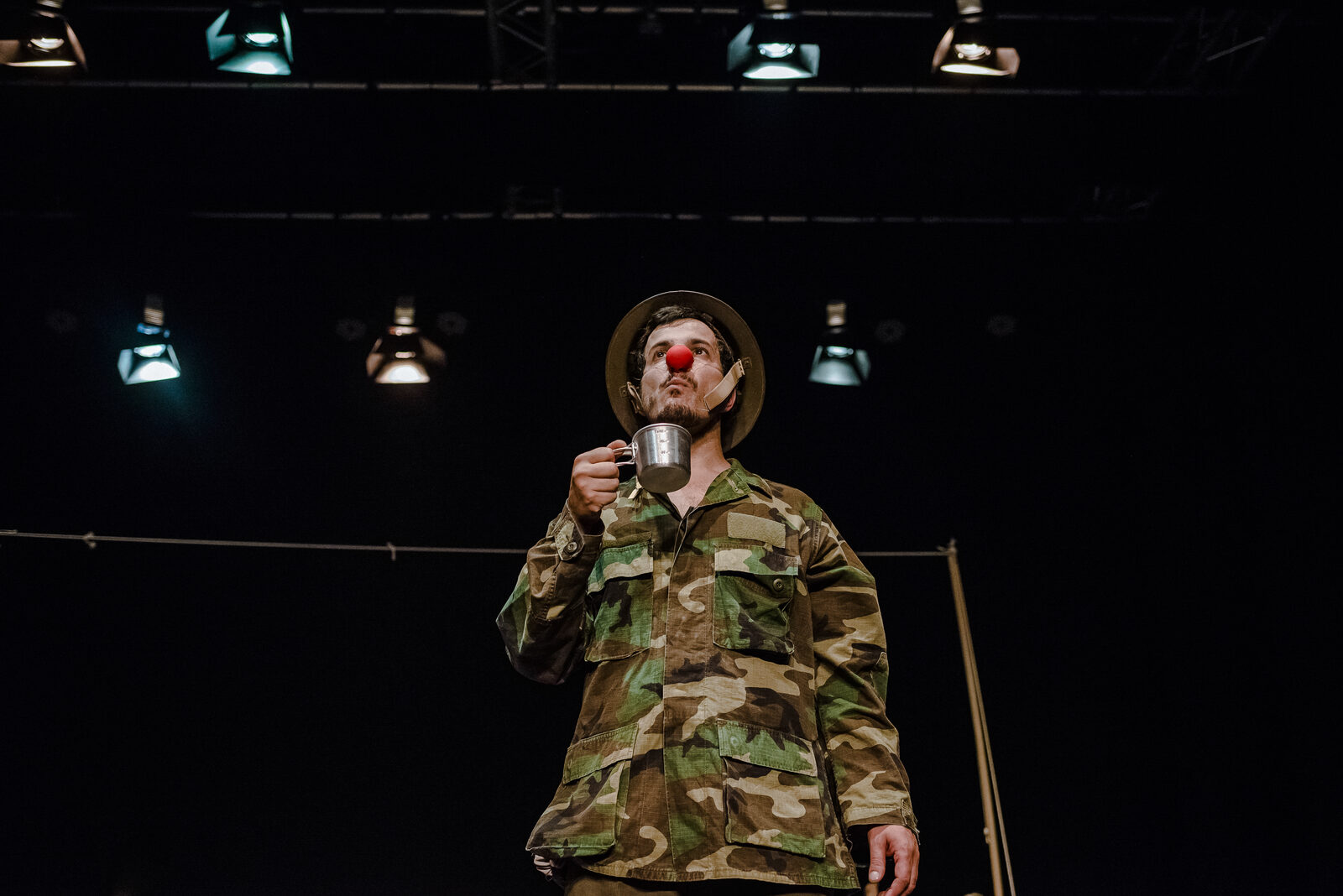 Clown amb nas vermell i jaqueta de camuflatge, en un escenari fosc